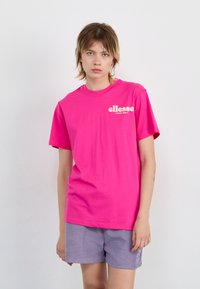 T-shirt en coton rose vif avec un col rond et des manches courtes ; comporte un logo blanc sur la poitrine gauche. Texture lisse.