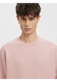 Lys rosa strikkegenser med rund hals, med en myk tekstur og en avslappet passform. Ingen synlige mønstre eller pynt.