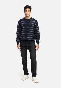 Marine gestreepte sweater met beige horizontale lijnen, geribbelde manchetten en zoom, gecombineerd met zwarte jeans en witte sneakers.