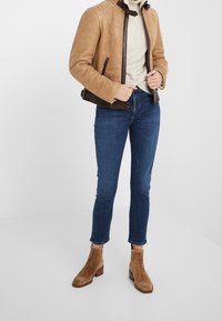 Tan mockaskinnbombarjacka med bruna läderdetaljer, gräddfärgad polo, mörkblå skinny jeans och bruna mockasiner med blockklack.