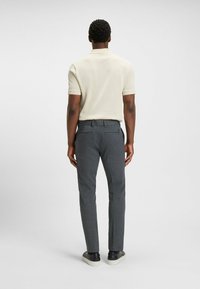 Polo shirt in light beige, short sleeves. Gray tailored trousers with a subtle pattern, rear pockets, paired with black sneakers.