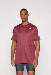 Camiseta deportiva color marrón burdeos, de manga corta, con cuello redondo, hecha de una tela suave. Presenta un logo blanco en el lado izquierdo del pecho y en la manga.