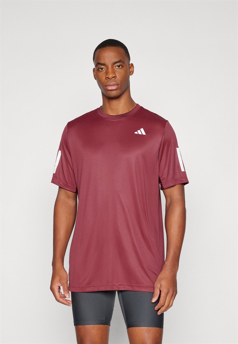 Camiseta deportiva color marrón burdeos, de manga corta, con cuello redondo, hecha de una tela suave. Presenta un logo blanco en el lado izquierdo del pecho y en la manga.