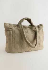 Sac fourre-tout beige matelassé avec deux poignées, présentant un motif texturé de cercles et de carrés. Design simple et élégant sur un fond clair.