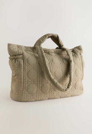 Quiltet beige tote bag med to håndtag, der har et struktureret mønster af cirkler og firkanter. Enkel, stilfuld design på en lys baggrund.