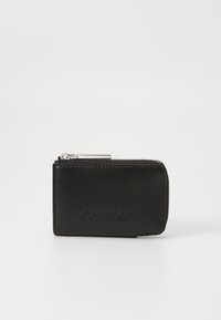 Portafoglio in pelle nera con una superficie liscia, chiusura con zip e logo "Calvin Klein" in rilievo sul davanti. Design rettangolare compatto.