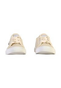 Zapatillas de lona beige con suelas de goma blanca, puntera redonda, cordones en la parte frontal y detalles texturizados en la puntera y el talón.