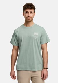 T-shirt en coton vert menthe avec un petit imprimé graphique blanc sur la poitrine gauche. Manches courtes et coupe droite.