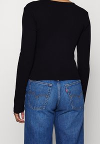 Schwarzes Langarmoberteil, kombiniert mit hellblauen, hoch taillierten Jeans, die auffällige Gesäßtaschen und kontrastierende Nähte aufweisen.