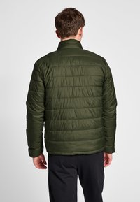 Olivengrøn pufferjakke med quiltet mønster, der har en stående krave og elastiske manchetter. Letvægtsmateriale, almindelig pasform.