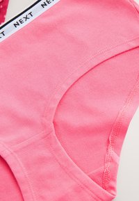 Sous-vêtement en coton rose avec une ceinture élastique blanche présentant le texte noir répété "NEXT".
