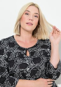 Top de estampado en blanco y negro con escote en forma de lágrima y mangas de tres cuartos. La tela parece ligera y tiene una textura suave.