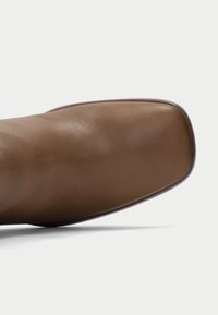 Zapato de cuero marrón con punta redondeada, textura suave y costuras mínimas. La suela está ligeramente elevada, proporcionando una apariencia aerodinámica.