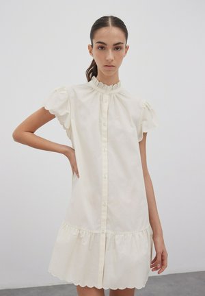 Robe en coton blanche avec des manches courtes bouffantes, un col froncé haut, une fermeture à boutons sur le devant et un ourlet festonné.