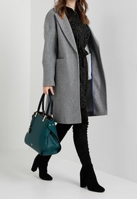 Cappotto grigio in lana con vestibilità rilassata e rever a punta, abbinato a un vestito nero con motivo leopardato e stivali neri in suede al ginocchio.