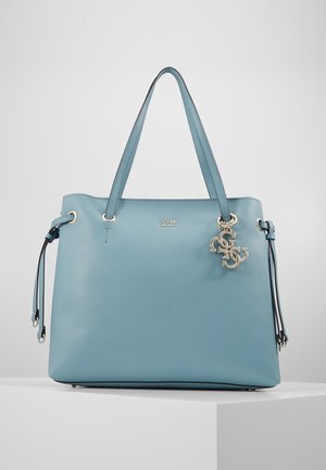 Jasnoniebieska skórzana torba typu tote marki Guess z podwójnymi uchwytami, bocznymi wiązaniami i metalowym zawieszonym logo blisko górnej krawędzi.