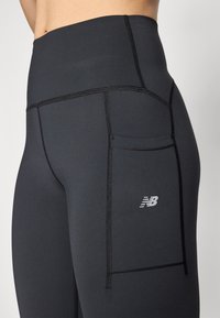 Leggings negre cu talie înaltă dintr-un material elastic, dotate cu o buzunară laterală și cusături contrastante. Logo-ul este afișat pe coapsa superioară.