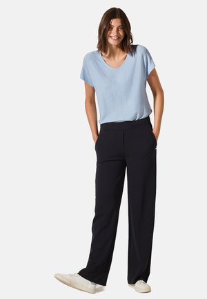 Ljust blå kortärmad topp med en texturerad yta, tillsammans med svarta vida byxor. Vita sneakers fulländar outfiten.