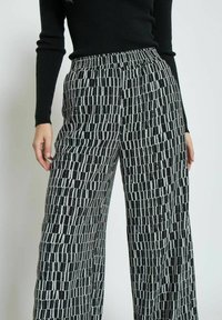 Black and white patterned wide-leg trousers with an elastic waistband, featuring a geometric design of vertical and horizontal stripes.