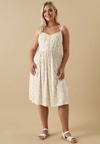 Kwiatowa sukienka midi w kolorze kremowym, z cienkimi ramiączkami, zapinana na guziki z przodu i elastycznym pasem. Ozdobiona małymi różowymi i pomarańczowymi kwiatkami.
