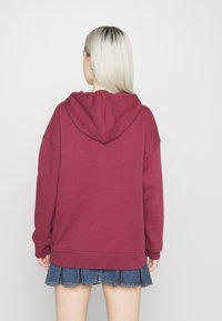 Felpa bordeaux con una vestibilità rilassata, cappuccio centrale e maniche lunghe. Abbinata a una gonna di jeans con orlo sfrangiato.
