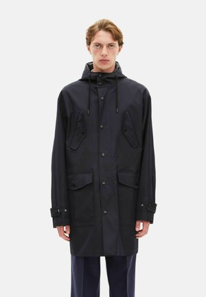 Parka imperméable navy avec capuche, quatre poches, boutons-pression et cordons de serrage. Présente une texture lisse et des poignets ajustables.