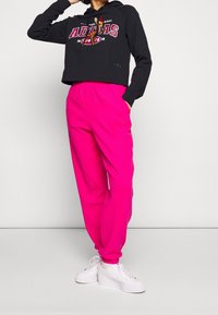 Black cropped hoodie with red graphic text and drawstrings, paired with bright pink ribbed joggers and white sneakers.