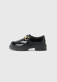 Black leather loafer with chunky sole and gold buckle detail, shown in profile against a light gray background.