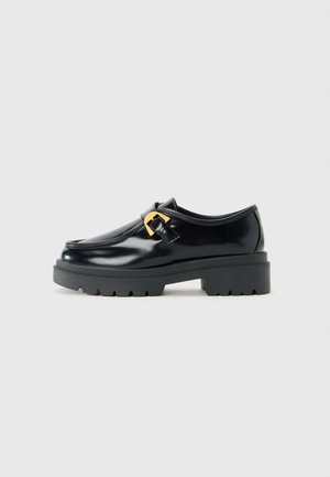Black leather loafer with chunky sole and gold buckle detail, shown in profile against a light gray background.
