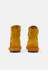 Botines de ante amarillos con un tacón ligeramente elevado, que presentan una textura suave, punteras redondeadas y una cremallera en el lado exterior.