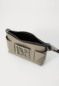 Grau vegan Leder Crossbody-Tasche mit strukturierter Oberfläche, ausgestattet mit einem silbernen Logo-Akzent und einem schwarzen Reißverschluss, einschließlich Seitentaschen.