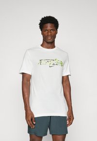 Biela tričko s grafikou "JUST DO IT" v zelenej a šedej farbe a logom Nike, s krátkymi rukávmi a dizajnom s okrúhlym výstrihom.