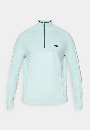 Šviesiai mėtinis žalias zip-up džemperis su aukštu apykakle, tekstūruota mezgimo medžiaga ir juodu logotipo akcentu ant krūtinės. Ilgos rankovės su raukšlėmis.