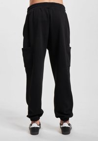 Sorte joggebukser med et teksturert sidepanel, elastisk midje og mansjetter. Har to sidelommer, kombinert med svarte og hvite joggesko.