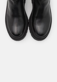 Botas de tobillo de cuero negro con un acabado liso, punta redondeada y suela de goma negra gruesa, presentando un diseño minimalista sin herrajes visibles.