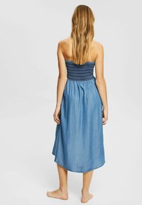 Denim maxiklänning med smockad överdel, mjuk blå färg, semiåtsittande design och en flödande fåll. Öppen ryggdetalj, ärmlös.