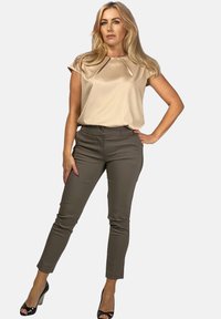 Beżowy top przypominający jedwab, z krótkimi rękawami i plisowanym dekoltem, w połączeniu z dopasowanymi oliwkowymi spodniami i czarnymi szpilkami.