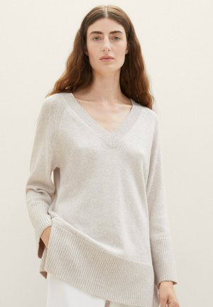 Pull col V couleur beige clair en tricot doux. Fit décontracté, avec des poignets côtelés et un ourlet arrière plus long. Design simple et texturé.