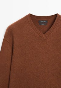Bruin wollen trui met V-hals, geribbelde kraag en zichtbaar merklabel bij de halslijn.