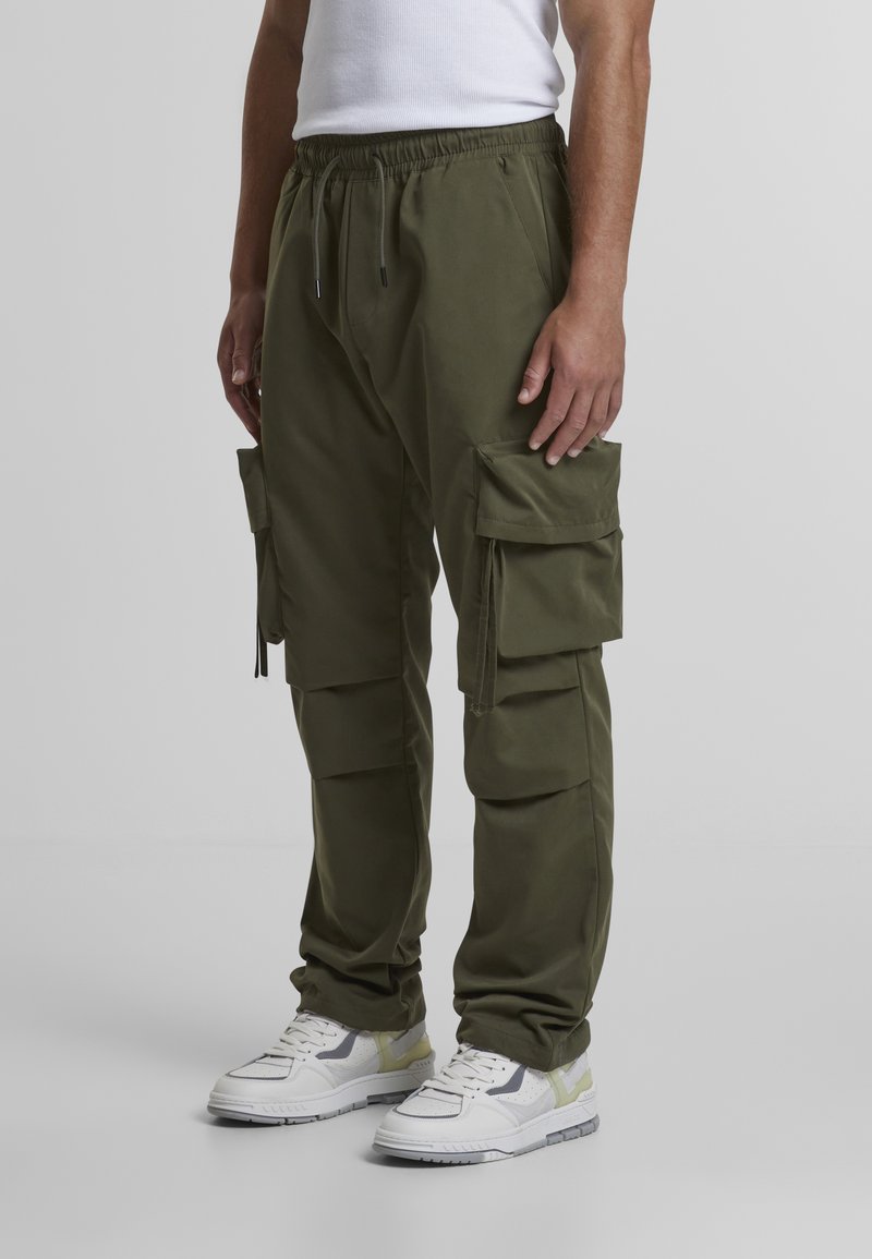 Olive green cargo pants with elastic waistband and multiple side pockets, made of lightweight fabric. Paired with white sneakers.