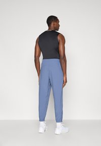 Μαύρο αμάνικο τοπ και μπλε αθλητική παντελόνι με ελαστικούς αστραγάλους, σε συνδυασμό με λευκά αθλητικά παπούτσια και ορατές κάλτσες έως τον αστράγαλο.