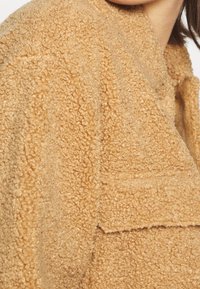 Giacca in pile beige con superficie testurizzata e pelosa, dotata di colletto a revers e tasca a toppa sul fronte.