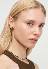 Guld geometriska örhängen har rektangulära former. Halsbandet har fyrkantiga länkar som kompletterar örhängena med en glänsande finish.