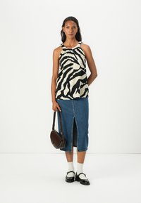 Top senza maniche con stampa zebra bianca e nera, gonna di jeans con spacco frontale, abbinata a una borsa a tracolla scura e scarpe nere con calzini bianchi.