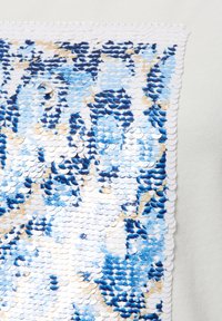 Sequin top with blue, white, and gold circular sequins arranged in a textured pattern, bordered by white fabric with a scalloped edge.