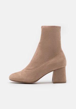 Bottes basses en daim beige avec un talon carré, un bout arrondi, une texture lisse et des détails cousus sur les côtés.