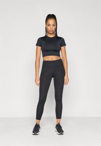 Μαύρο αθλητικό crop top και ψηλόμεσα κολάν, με λεία υφή και εφαρμοστή σχεδίαση, συμπληρωμένα με μαύρα αθλητικά παπούτσια.