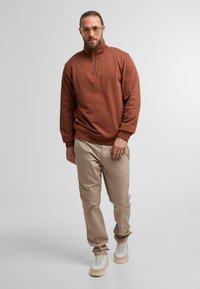 Brun lynlås sweatshirt med høj krave, parret med beige bukser og hvide sneakers. Glat stof med ribbede manchetter og kant.