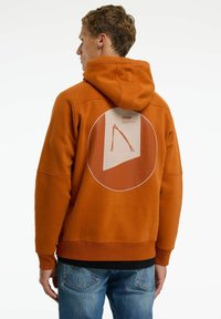 Oranje hoodie met een cirkelvormige grafiek op de achterkant, met een rasterpatroon en een gestileerd ontwerp in een contrasterende kleur.