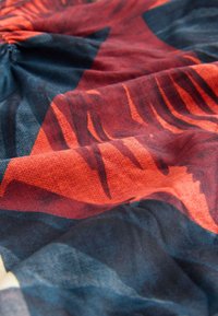 Tkanina w wzory z wyrazistymi pomarańczowymi i ciemnoniebieskimi geometrycznymi kształtami o fakturowanym splocie. Miękki, lekki materiał.